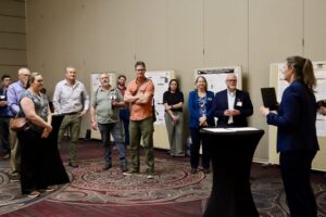 11 people in a presentation room surrounded by academic posters.