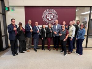 13 people standing underneath the Texas A&M University System seal outside of the Nuclear Security Office on Texas A&M University.