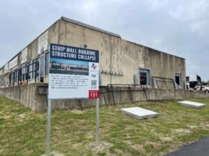 A concrete building with a sign "Strip Mall Building Structure Collapse" on the sign.
